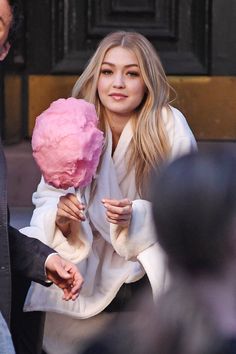 a blonde woman holding a pink flower in her right hand while walking down the street