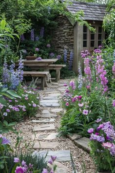 a garden with purple flowers and a stone path leading to a picnic table in the middle