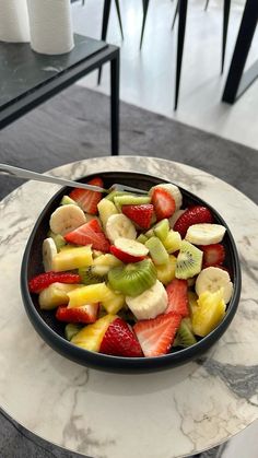 a bowl filled with sliced up fruit on top of a marble dining table next to a black chair