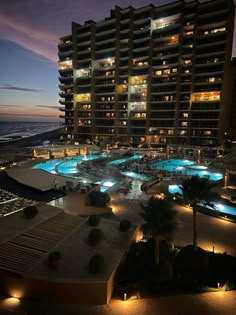 an outdoor swimming pool at night next to a large building with multiple balconies