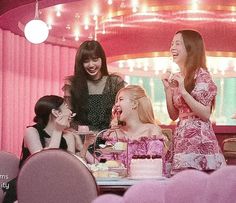 three women sitting at a table eating cake and drinking tea together in a pink room