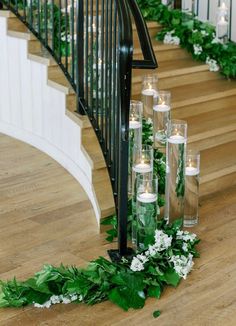 candles are lined up on the floor next to flowers and greenery