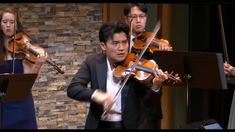 a man playing the violin in front of two women and one man standing behind him