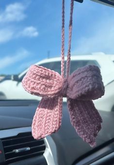 a pink knitted bow hanging from the dashboard of a car