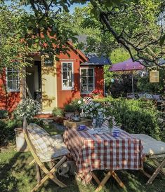 an outdoor table and chairs in front of a small red house with flowers on it