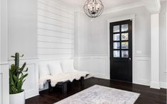 a white room with wood floors and a black door in the center, along with a large rug on the floor