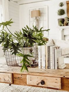 a table topped with books and plants on top of a wooden table next to a bed