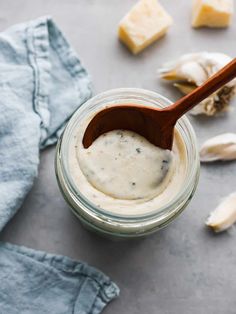 a wooden spoon is in a jar filled with cream cheese spread and sliced garlic on the side