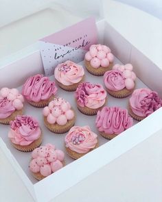 a box filled with pink frosted cupcakes on top of a white table