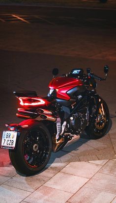 a red motorcycle parked on top of a street next to a parking meter at night