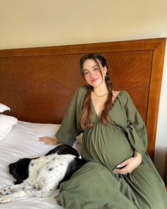 a pregnant woman sitting on top of a bed next to a dog