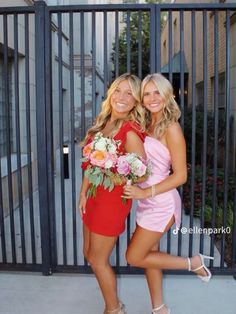 two beautiful young women standing next to each other in front of a black metal fence