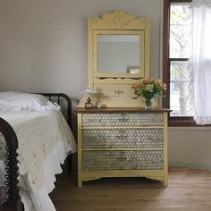 a bedroom scene with focus on the dresser and bed in the foreground, and an open window to the outside