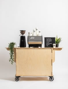 a wooden cart with coffee machines on top and plants in the middle, against a white background