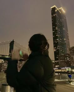 a woman looking at her cell phone in front of a cityscape and bridge