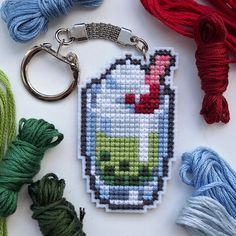 a cross stitch keychain that has some yarn and scissors on the table next to it