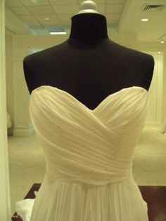 a white dress on display in a room with a black mannequin behind it