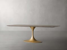 an oval dining table with gold legs and a marble top, against a grey background