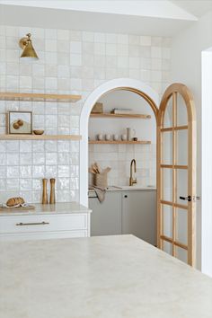 a white kitchen with open shelves and wooden doors leading to the dining room, next to an arched doorway