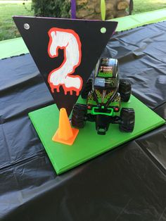 a monster truck birthday cake on top of a black table cloth with green and orange decorations