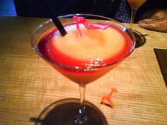 a red drink in a glass on a table with a person sitting at the table