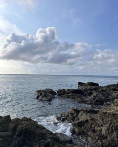 an ocean view with rocks in the foreground and clouds in the sky above it