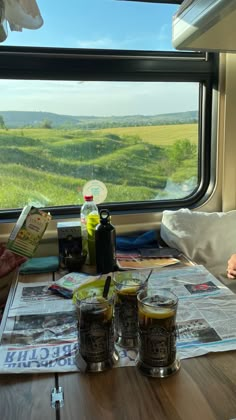 a table with drinks and magazines on it in front of a window overlooking the countryside