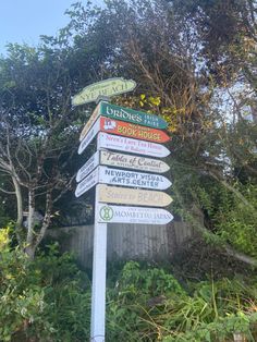 a pole with many different signs on it in front of trees and bushes near a fence