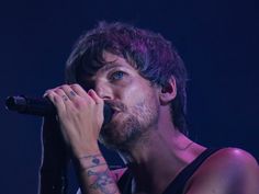 a man with tattoos on his arm holding a microphone in front of him and looking up at the sky