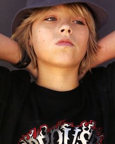 a young boy wearing a black shirt and hat with his hands behind his head,