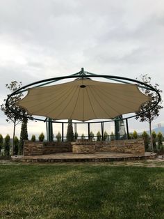 an outdoor gazebo in the middle of a grassy area with trees and bushes around it