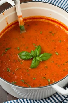 a bowl of tomato soup with basil on top and croutons in the background