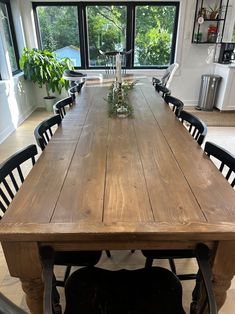 a large wooden table with chairs around it in front of a window and potted plants