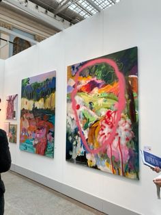 people looking at paintings on display in an art gallery, one woman is holding a book