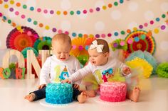 two babies are sitting next to each other in front of a birthday cake and decorations