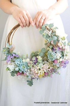 a woman holding a wreath with succulents and greenery in her hands