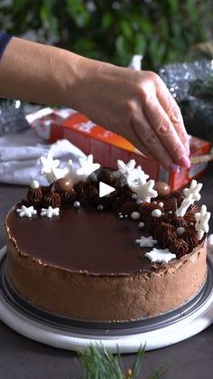 a person is decorating a chocolate cake with white frosting and sprinkles