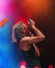 a man with long hair holding a microphone up to his mouth while standing on stage