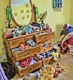 the dresser is full of clothes and clutter in front of a large round mirror