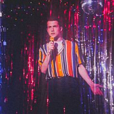 a man holding a microphone in front of a disco curtain