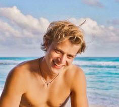 a shirtless young man sitting on top of a sandy beach next to the ocean