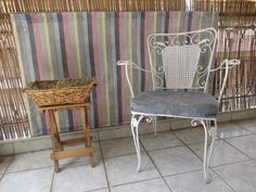 a white chair sitting next to a basket on top of a wooden table in front of a striped wall