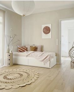 a bedroom with white walls and wooden floors is pictured in this image, there is a round rug on the floor next to the bed