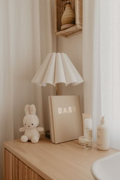 a white teddy bear sitting on top of a wooden dresser next to a baby book