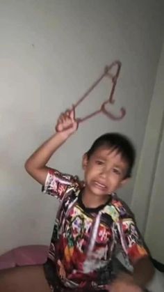 a young boy sitting on top of a bed holding up a pair of scissors above his head