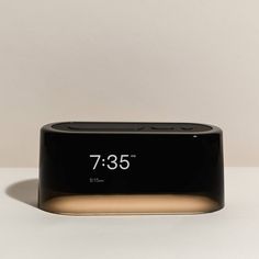 an alarm clock sitting on top of a white table next to a black and gold base