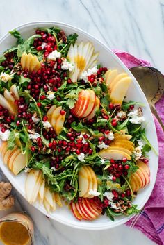 a white plate topped with apples, spinach and pomegranate on top of a table