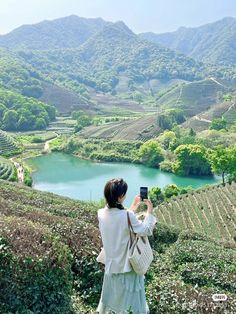 a woman taking a photo with her cell phone in front of a lake and mountains