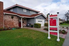 a red and white for sale sign in front of a gray house with two garages