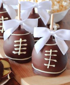 chocolate covered candies with white ribbons and bows are on a wooden board next to bowls of popcorn